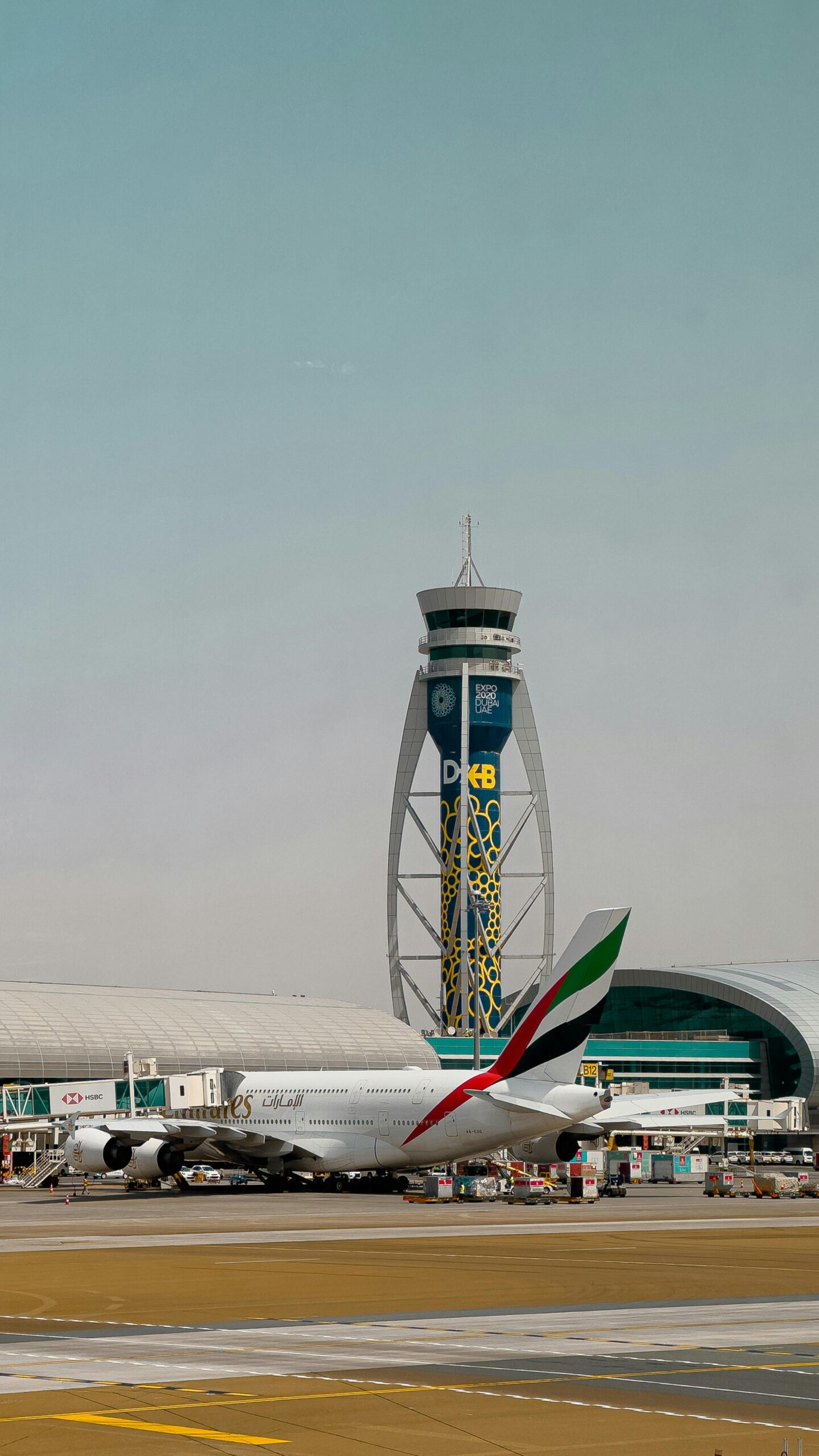 Emirates airplane on tarmac with Dubai's iconic ATC tower at DXB under a clear sky.